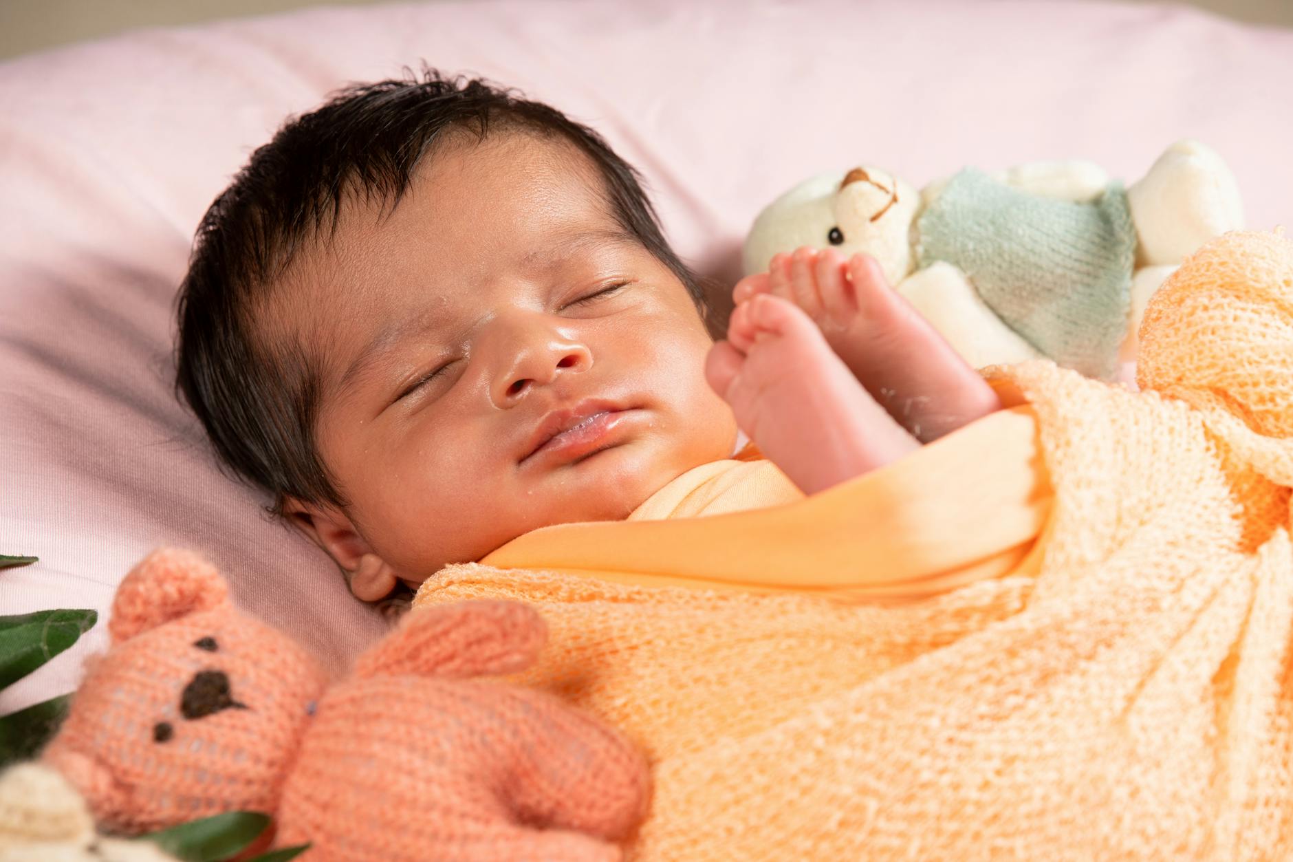 Adorable newborn baby sleeping with soft toys, wrapped in a cozy blanket indoors.
