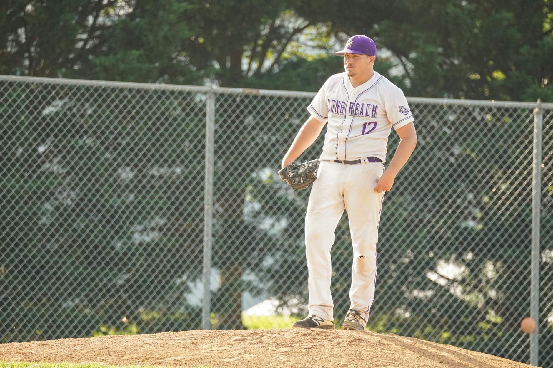 Baseball player in uniform preparing to pitch on a sunny day at an outdoor field.