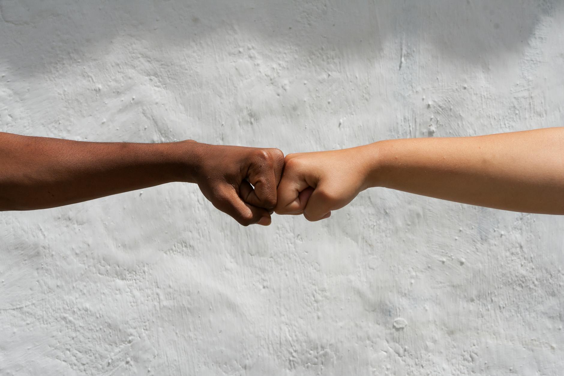 Two diverse hands performing a fist bump against a white wall, symbolizing unity and friendship.