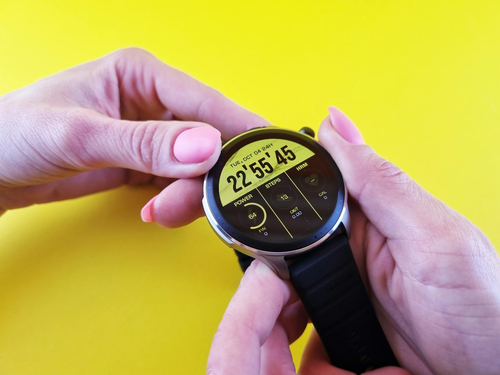 Close-up of hands holding a sleek smartwatch, highlighting technology against a bright yellow background.
