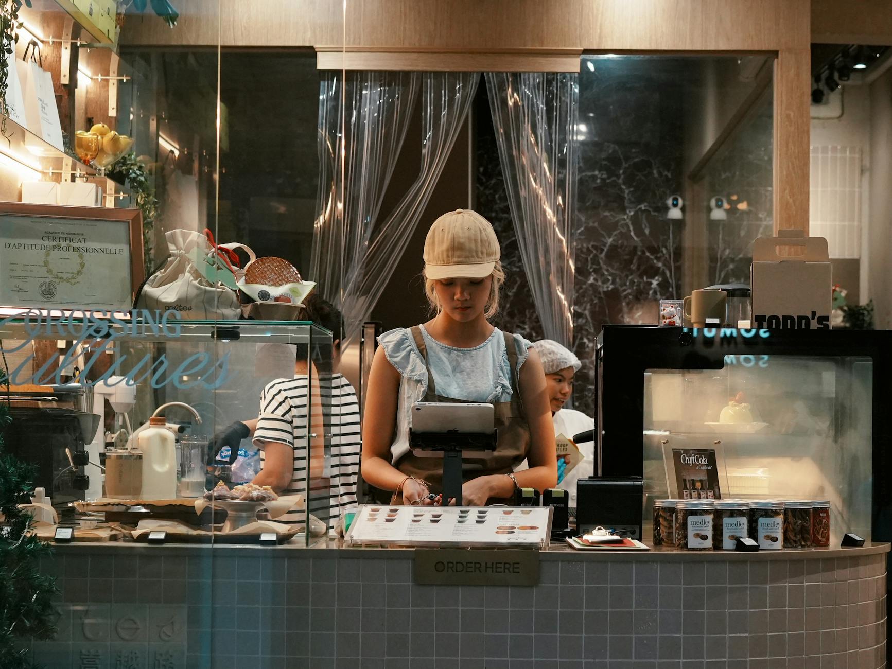 A young woman behind the counter at a modern bakery, engaging with a point of sale system.