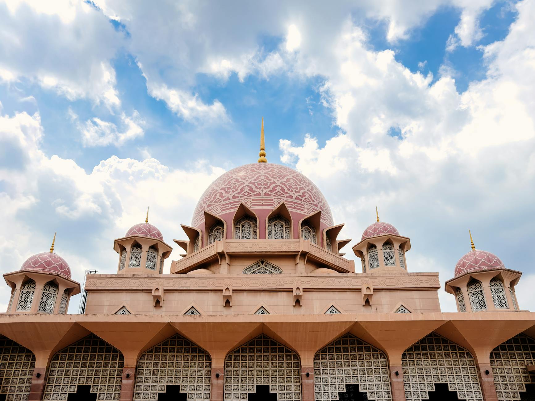 Elegant view of the iconic pink-domed Putra Mosque in Putrajaya, Malaysia under a bright blue sky.