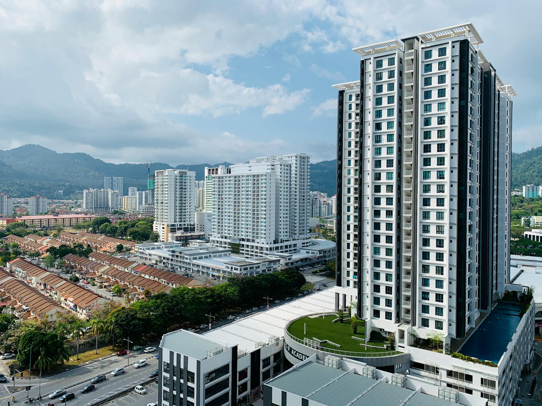 Modern tall geometric building with outdoor swimming pool and green sports ground located in new residential district of contemporary city against cloudy sky