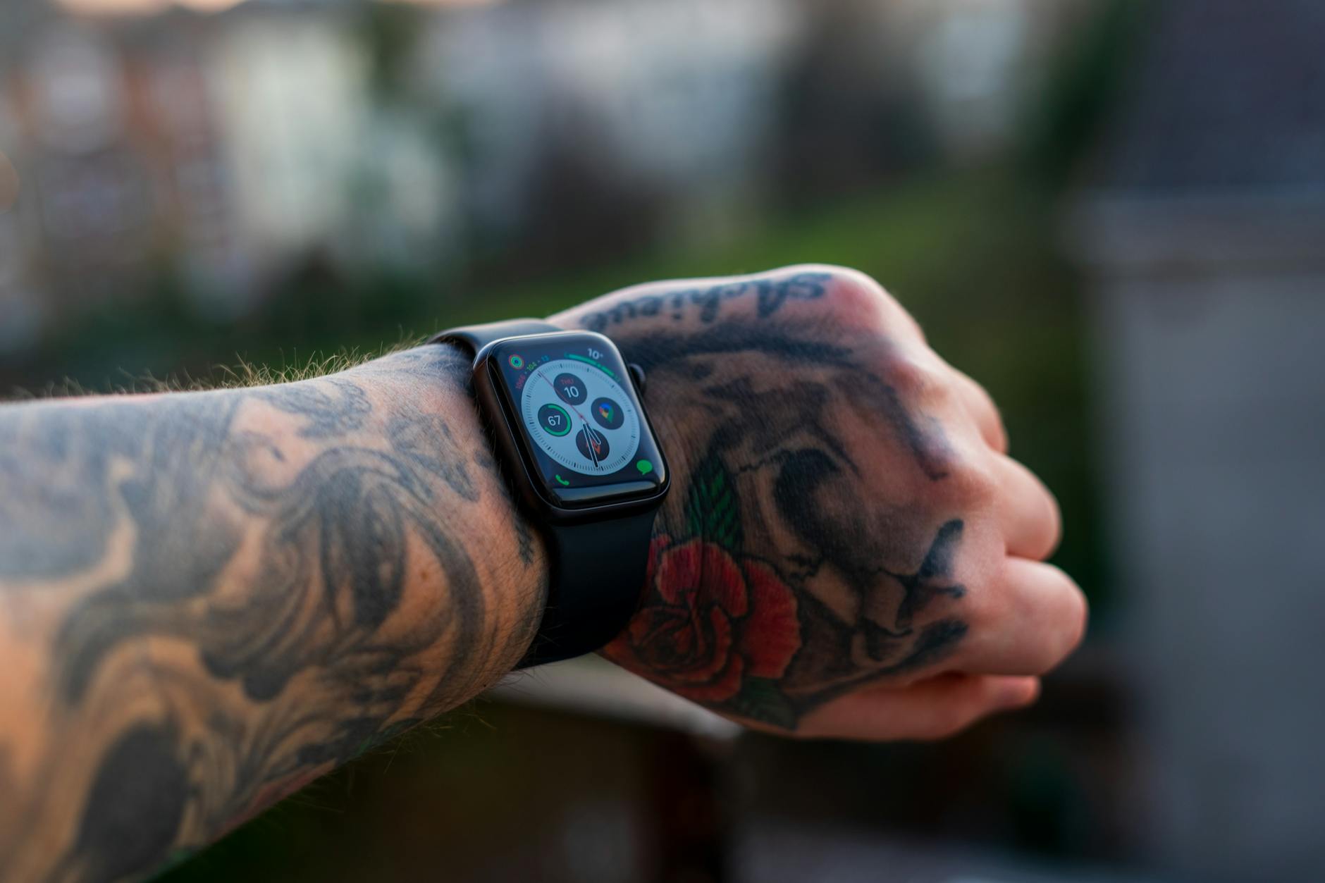 Close-up of a tattooed arm wearing a smartwatch outdoors, showcasing technology and personal style.