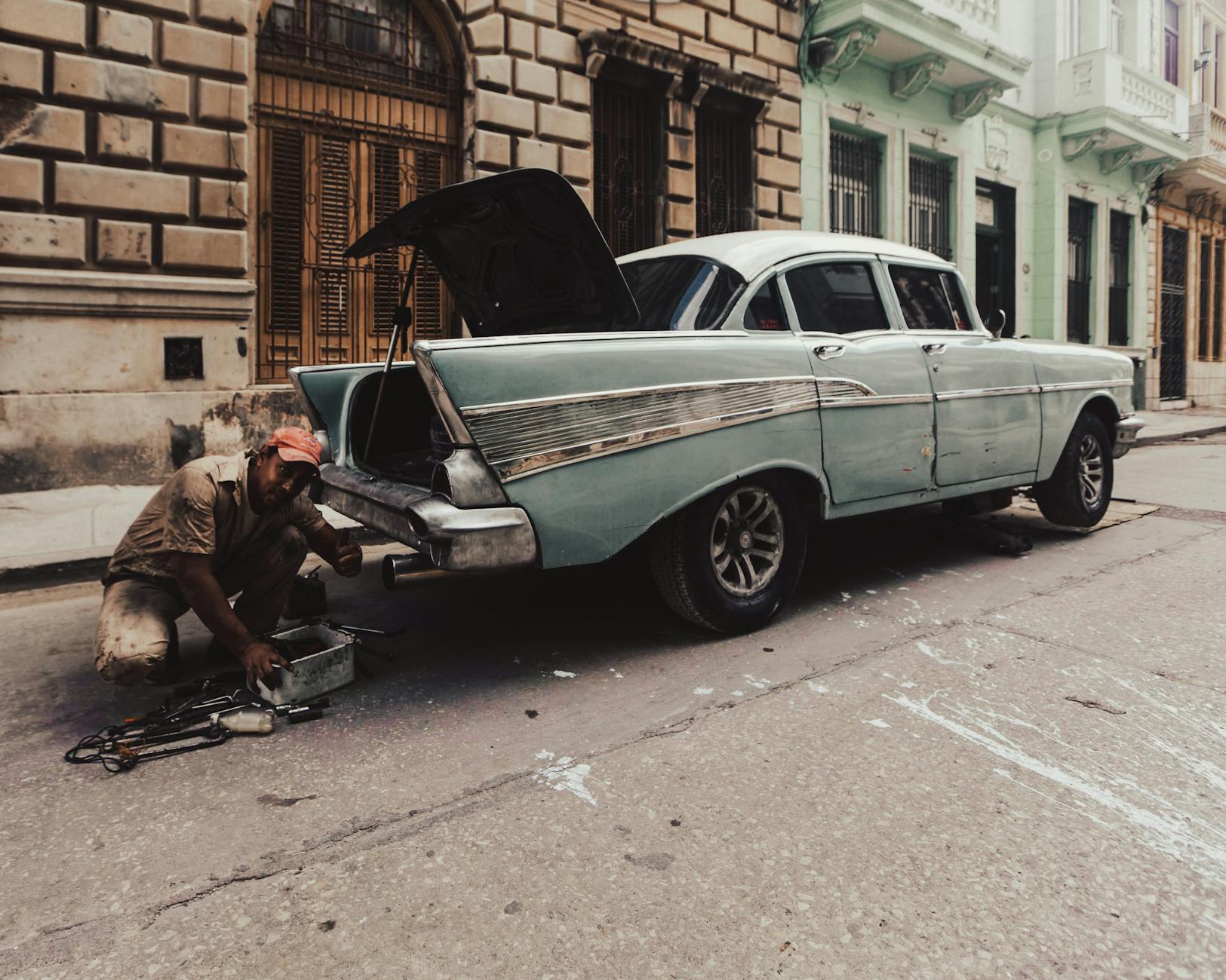 A man fixing a classic car on the street, focusing on maintenance and vintage automotive style.