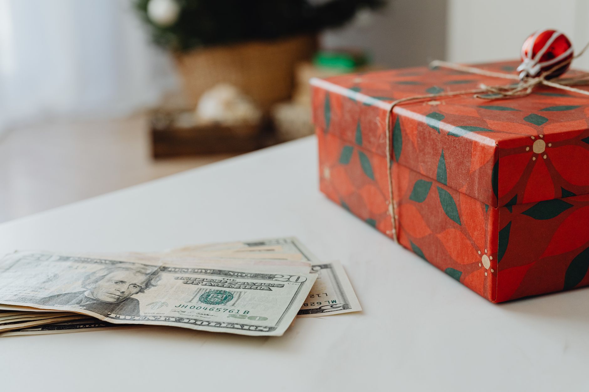 Red festive gift box with US dollar bills on a table, ideal for holiday-themed uses.