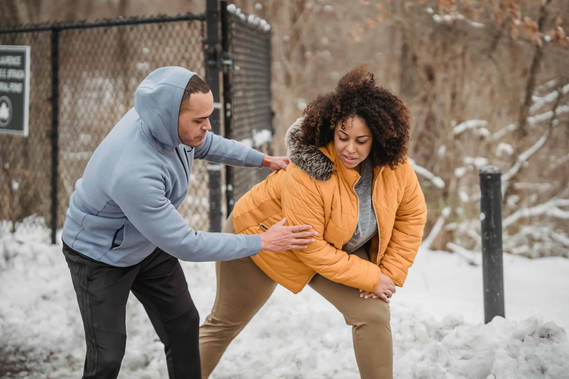 African American trainer helping plus size black woman to do stretching exercise while standing in winter park with snow during training