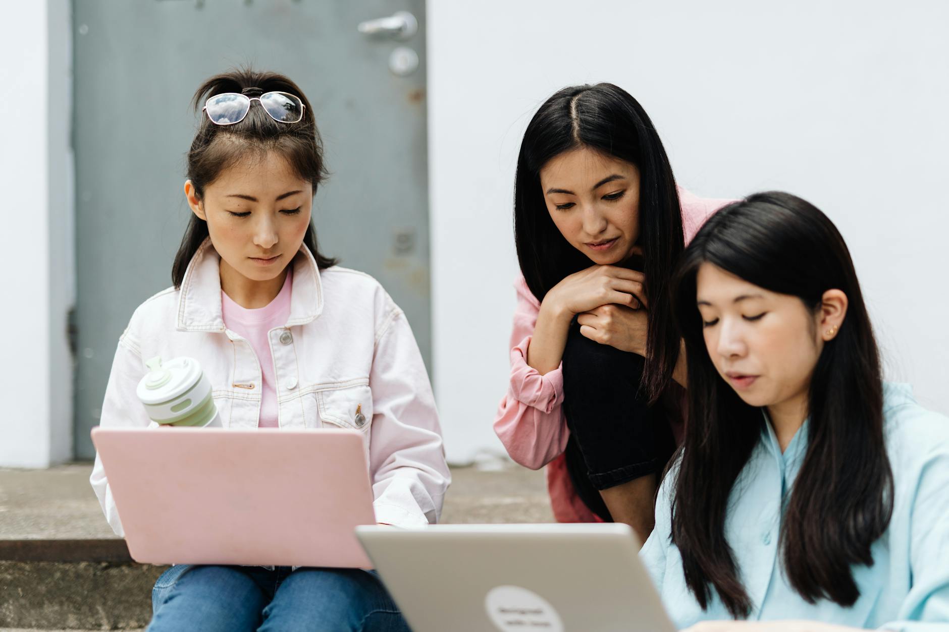 Three young Asian women working together on laptops outdoors, highlighting education and technology.
